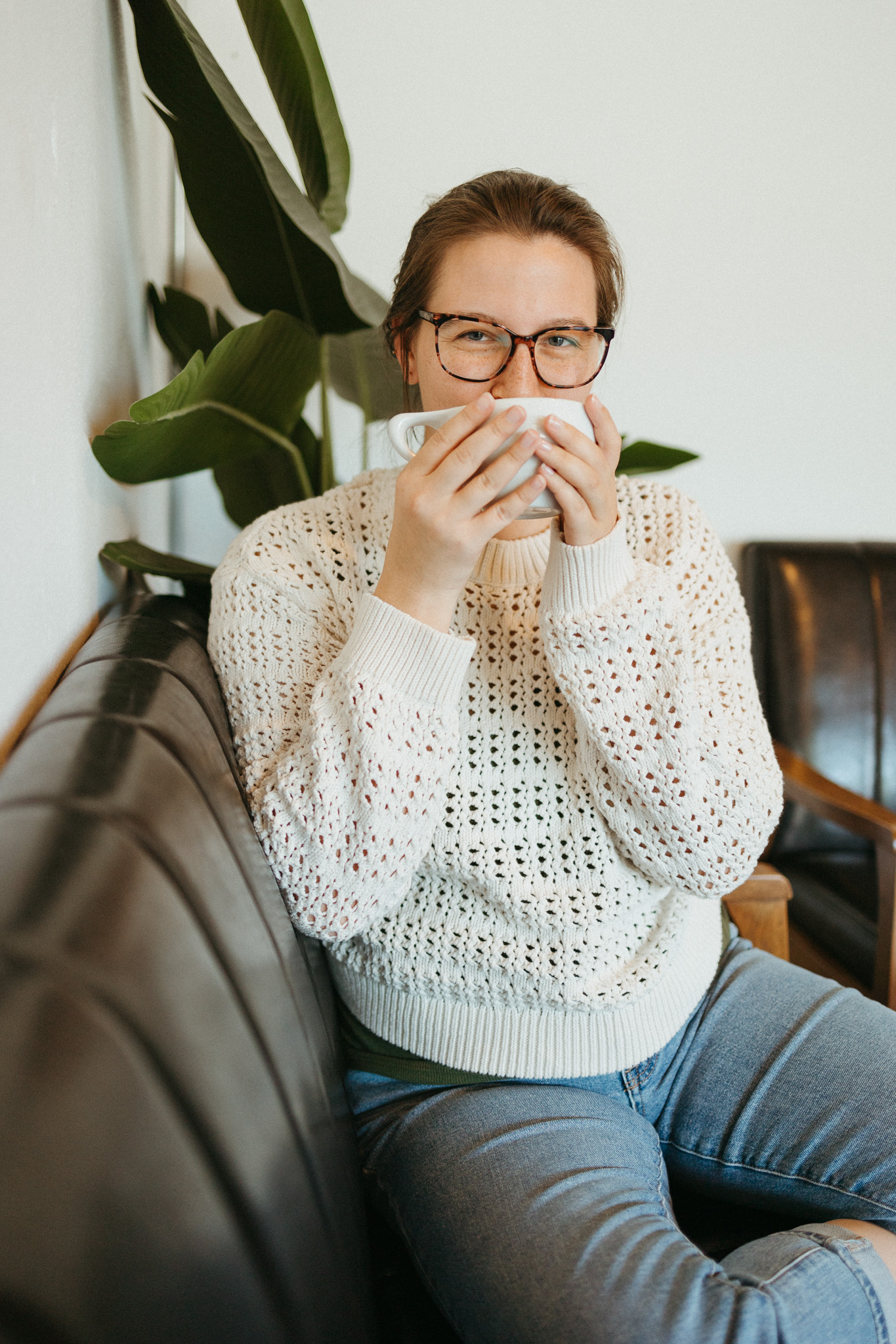 seo strategist and blog content writer wearing an off-white crochet top sipping coffee on a brown couch